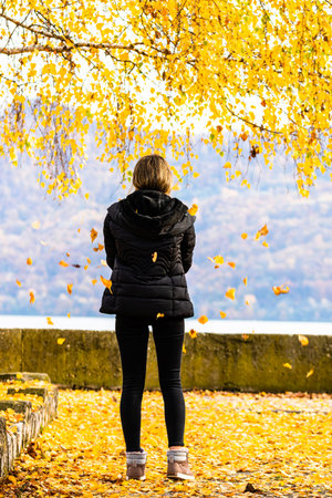 Autumn leaves fallen on alone woman walking on the autumn alley