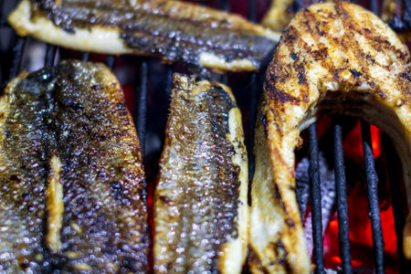 Fresh fish fillets cooking on a hot barbecue grill with smoke and fire flames for healthy outdoor...