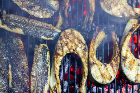 Fresh fish fillets cooking on a hot barbecue grill with smoke and fire flames for healthy outdoor picnicの写真素材