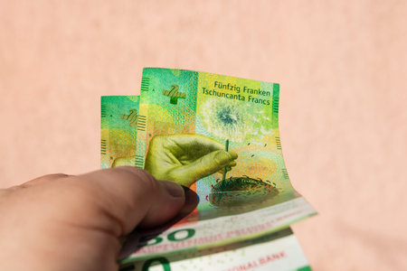 Man hand holding Swiss Franc money banknotes, showing paper texture and symbols of Swiss CHF...