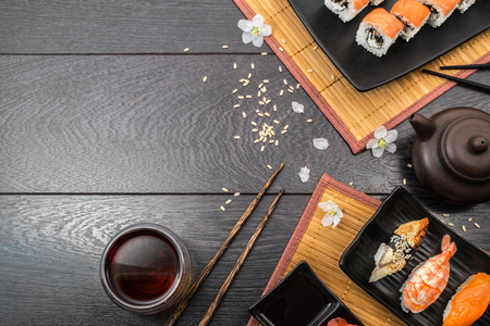 Sushi set sashimi, nigiri, maguro and sushi rolls served on plate with teapot and white flowers on dark wooden background. Space for text.の写真素材