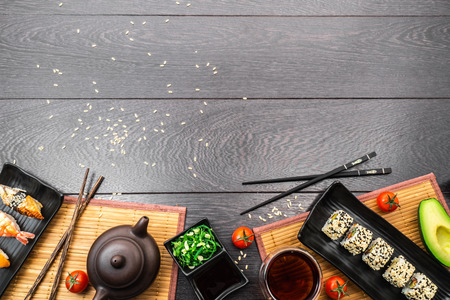 Sushi set sashimi, nigiri, maguro and sushi rolls served on plate with teapot and tomatoes on dark wooden background. Space for text.の写真素材