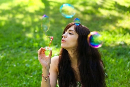 portrait of attractive young girl inflating colorful soap bubbles outdoorの写真素材