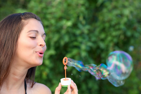 portrait of attractive young girl inflating colorful soap bubbles outdoor