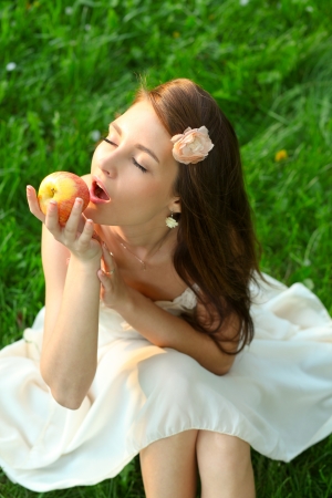 Adorable happy young lady with beautiful sappy apple over green grassの写真素材