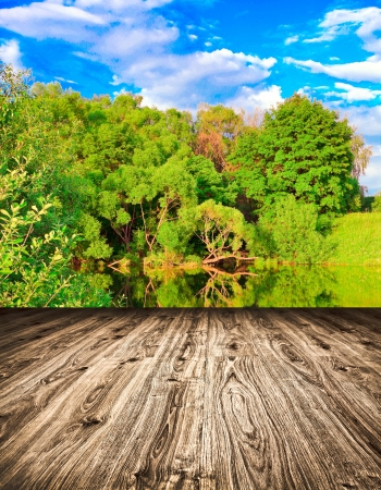 Light picturesque scene of beautiful rural lake in sunny summer park over blue sky with first dawn rays on the wall inside room interior with frame textured wooden brown panel floor backgroundの写真素材