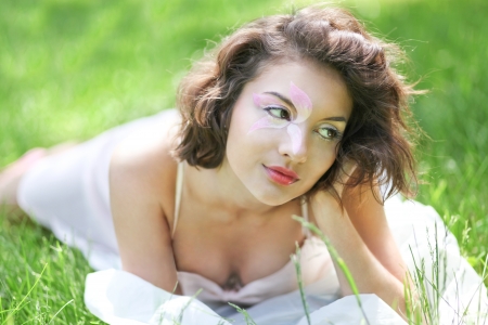 Portrait of Gorgeous young pretty brunette woman relaxing in sunny spring park in white cloth with beautiful curly hair on bright green grass layingの写真素材