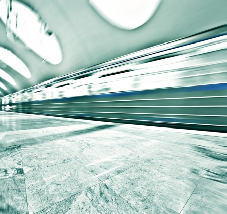 Perspective wide angle view of modern light blue illuminated and spacious public metro marble station with fast blurred trail of train in vanishing traffic motionの写真素材