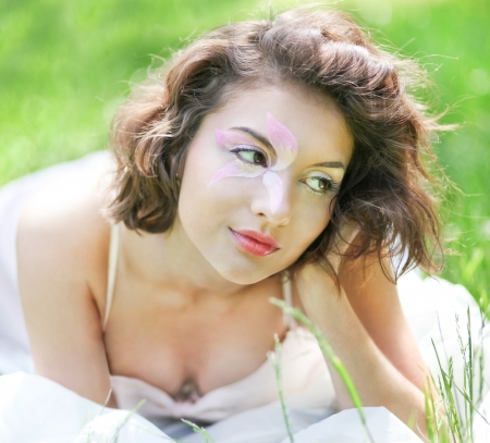 Portrait of Gorgeous young pretty brunette woman relaxing in sunny spring park in white cloth with beautiful curly hair on bright green grass layingの写真素材
