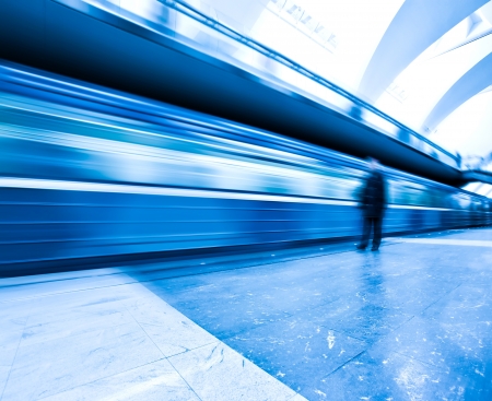 Perspective wide angle view of modern light blue illuminated and spacious public metro marble station with fast blurred trail of train in vanishing traffic motionの写真素材