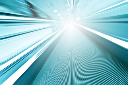 Perspective wide angle view of modern light blue illuminated and spacious high-speed moving commercial escalator with fast blurred trail of handrail in vanishing traffic motion in airport corridorの写真素材