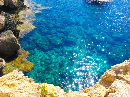View to a rocky beautiful coast among blue bright transparent water of the sea with sky reflection in sunny dayの写真素材