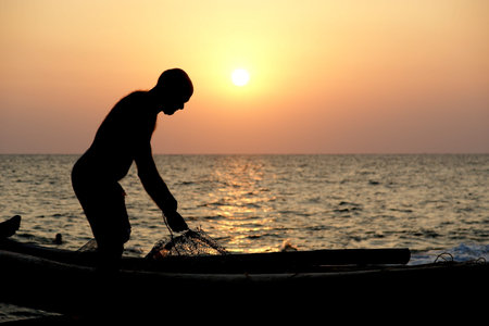 A fisherman with a boat on the ocean shore at sunset. Kerala, India