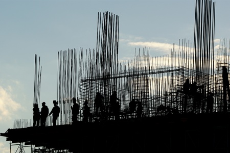The silhouettes of construction workers, construction equipment and elements of a building under construction at Sunsetの写真素材