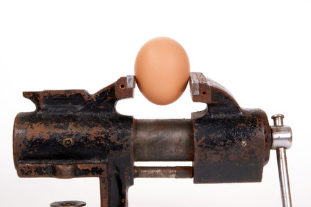 Egg trapped in the old rusty metalwork vice, on a white backgroundの写真素材