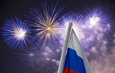 Celebratory colorful fireworks exploding in the skies and Russia flag waving in the wind against the sky. Three colors of Russian wavy flag as a patriotic symbolの写真素材