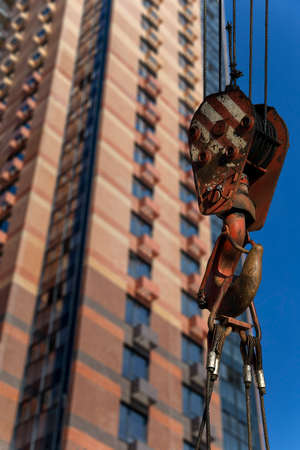 Construction crane hook with multi-storey building under construction (new residential complex) on the background. Construction site upon renovation program in Cheryomushki district, Moscow, Russiaの写真素材
