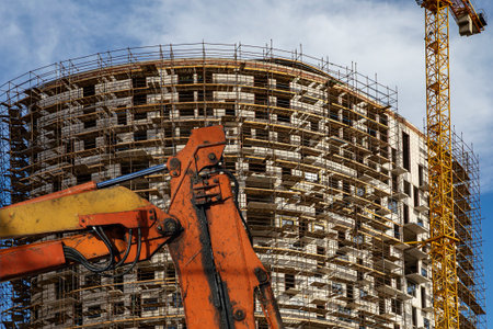 Part of a construction machine (excavator or crane) with multi-storey building under construction...