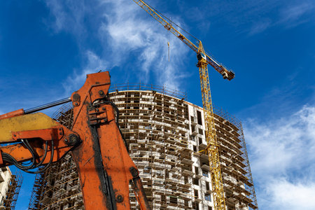 Part of a construction machine (excavator or crane) with multi-storey building under construction...
