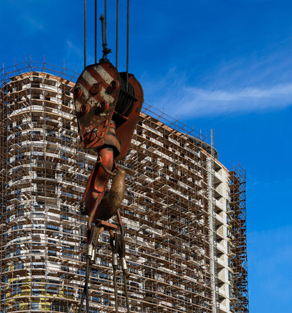 Construction crane hook with multi-storey building under construction with scaffolding (new...