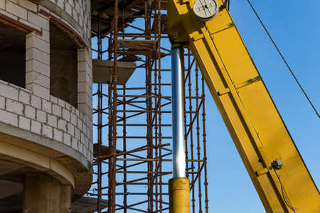 Part of a construction machine (excavator or crane) with multi-storey building under construction with scaffolding (new residential complex) on the background, Moscow, Russiaの写真素材