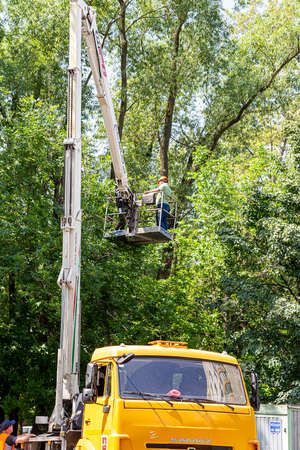 A car with a hydraulic lift plant in the courtyard of a residential building. Pruning dry branches, cutting down damaged trees, kroning. The work of city utilities. Moscowのeditorial素材