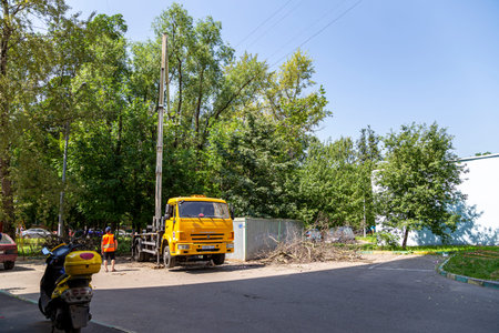 A car with a hydraulic lift plant in the courtyard of a residential building. Pruning dry branches, cutting down damaged trees, kroning. The work of city utilities. Moscowのeditorial素材