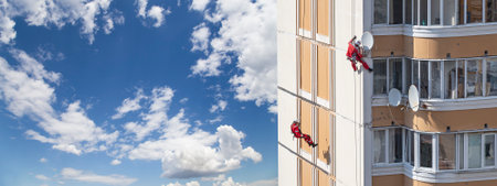 Repair work at height (sealing seams in a panel house), against the sky with clouds. Worker insulates the seams of the facade of an old residential building. Maintenance of residential buildingsの写真素材