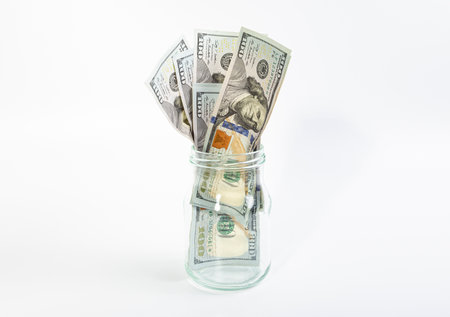 One hundred dollar bills in a glass jar, on a white backgroundの写真素材