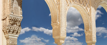 Arches in Islam (Moorish) style (against the background of a beautiful sky with clouds) in Alhambra,...