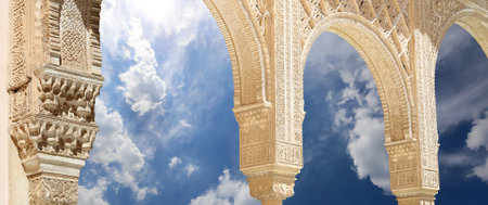 Arches in Islam (Moorish) style (against the background of a beautiful sky with clouds) in Alhambra,...