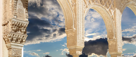 Arches in Islam (Moorish) style (against the background of a beautiful sky with clouds) in Alhambra,...
