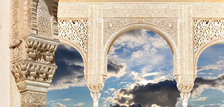 Arches in Islam (Moorish) style (against the background of a beautiful sky with clouds) in Alhambra,...