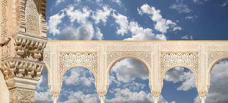 Arches in Islam (Moorish) style (against the background of a beautiful sky with clouds) in Alhambra,...