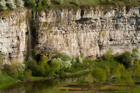 Spring landscape. The river flows in the valley along a natural stone wall with a waterfall.の写真素材
