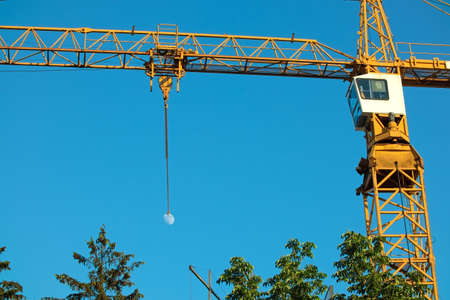 Construction crane on the background of the blue sky and the Moon. green tree topsの写真素材