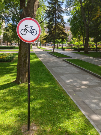 Sign in the summer city park. Bicycles are prohibited. Green grass on the lawn and alley in the park.の写真素材