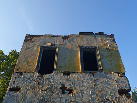 The facade of an old building that is collapsing against the blue sky. Broken windows of an old houseの写真素材