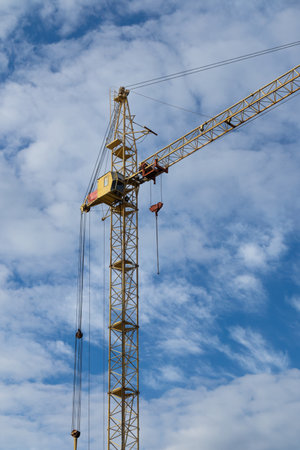 Tall yellow construction crane against a blue sky with clouds on a sunny day. construction machineryの写真素材