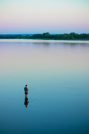Fisherman stands in the water and catches fish with a fishing rod. Wide river Dnieper, no waves