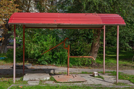 Manual water pump under a canopy in the yard. Close-up of a column for supplying drinking water. Trees and green grass in the backgroundの写真素材