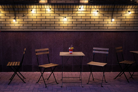Cafe tables and chairs on the sidewalk in the evening. Brick wall and electric lampsの写真素材
