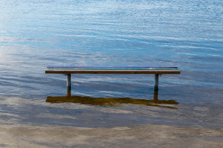 A wooden bench stands in the water during the day close-up
