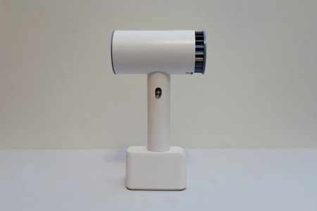 A white hair dryer with a rechargeable battery stands on a table on a white backgroundの写真素材