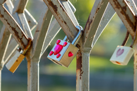 love lock or love padlock with pink hearts attached to a metal fence close-up on a sunny dayの写真素材