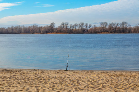 Fishing rod stands on the banks of the Dnieper river. Blue sky with clouds and forest on the horizonの写真素材