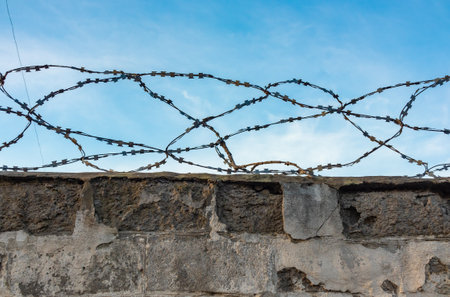 Barbed wire on an old fence close-up against the sky, the perimeter of a prison or a barrier on the border from illegal migrantsの写真素材
