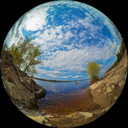 Fisheye circular photo of a river bank with rocks and trees on a sunny dayの写真素材