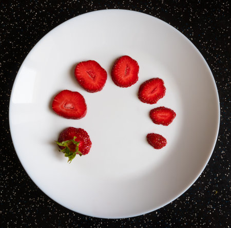 Sliced ripe strawberries on a white plate on the table, top viewの写真素材