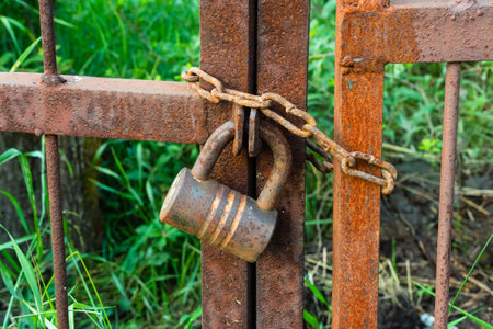 A large padlock hangs on a rusty gate against a backdrop of green grass. soft selective focusの写真素材
